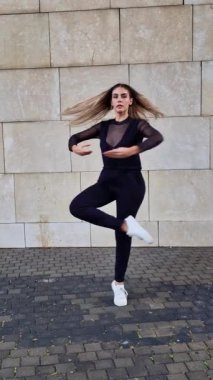 Çağdaş dansçı kentsel tuğla duvara karşı karmaşık bir modern koreografi sergiliyor, akışkan hareketler ve sanatsal yorumları dinamik enerji ve yaratıcı tutku ile ifade ediyor