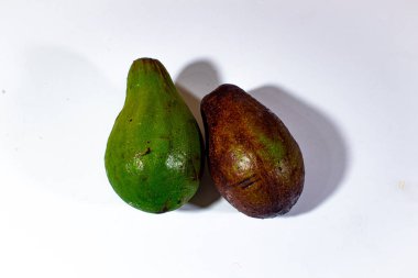 İki yeşil ve kahverengi avokado, sade beyaz arka planda sıralanmış.