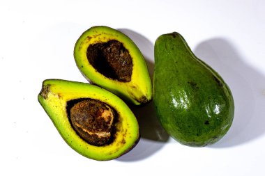 İki dilim avokado ve bir tane de beyaz arka plan üzerine yerleştirilmiş avokado.