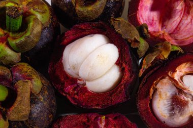 Bir fotoğraf nesnesinin ortasında taze beyaz renkli bir meyve dilimi olan taze mangosteen meyvesi var.