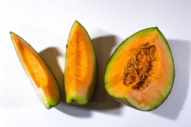 Sade beyaz arka planda servis edilen üç yeşil turuncu kavun.