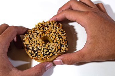 one donut with peanut and chocolate topping, held in two hands, on a plain white backgorund clipart