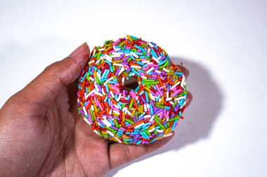 one donut with colorful sprinkle topping, held in the left hand, on a plain white backgorund clipart