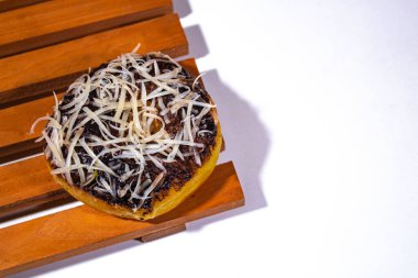 one donut with grated chocolate cheese topping, on a wooden coaster and a plain white backgorund clipart