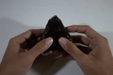 Geleneksel Japon yemeği, pirinçle doldurulmuş ve yosunlara sarılmış üçgen onigiri, sonra da düz beyaz bir arka planda iki elle tutulur.