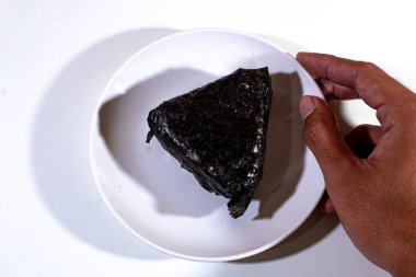 Geleneksel Japon yemekleri, pirinçle doldurulmuş ve yosunlara sarılmış üçgen onigiri, sol elde tutulan beyaz plastik bir tabakta servis edilir.