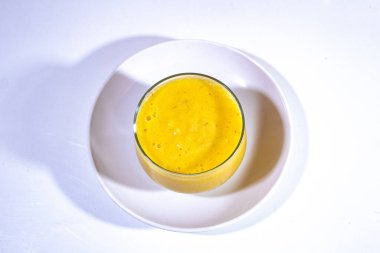 Bir mini cam bardak, ananas suyuyla dolu ve üzerinde beyaz plastik bir plaka var.