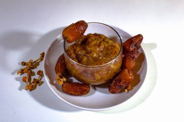 Hurma reçeli, cam bir bardakta ve plastik bir tabakta servis edilir, üstte ve yanlarda hurma ile süslenir.