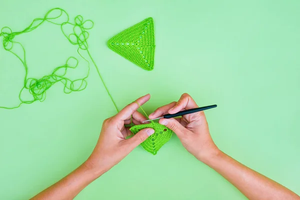 薄い緑の背景に緑の三角形のかぎ針編みのモチーフを作る手 かぎ針編みについてのシンプルでミニマリズム的な見解 — ストック写真