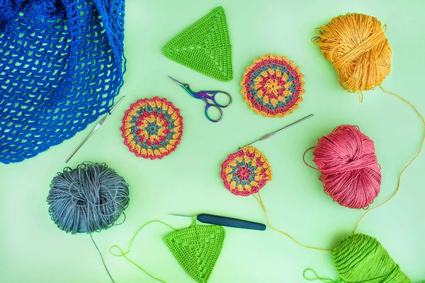 Layout of different crochet patterns, multicolored balls of yarn, hooks and scissors on light green background. Idea of crocheting different things.