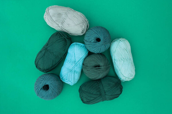 Top view of balls and skeins of different types of yarn in light blue, olive and dark green colors on green background. Concept of yarns with different texture in green tones.