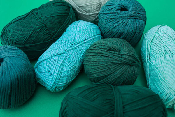 Close view of light turquoise skein of yarn surrounded with mainly dark green ones on green background. Balls of yarn with different texture.