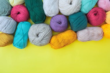 Parlak sarı arkaplan üzerine yerleştirilmiş farklı top ve iplik desenleri. Altında boşluk var. El yapımı için çok renkli lifler..