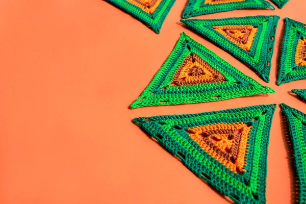 Right side is filled with big crochet triangles of green and orange color, left side is free, the background is a solid orange surface.