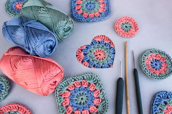 Crochet pattern in a heart and three different hooks with other patterns and skeins of yarn around on grey background. Love to crocheting.