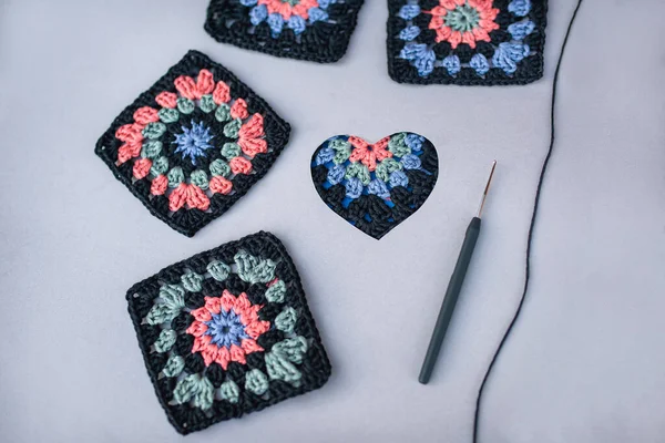 Granny squares with black boarder, crochet hook with black handle and crochet motif in a heart on grey background. Love to contrast  granny squares.