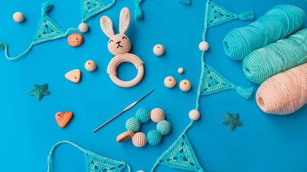 Layout of crochet baby toys, crochet hook and skeins of yarn on bright blue surface. Crochet for babies.
