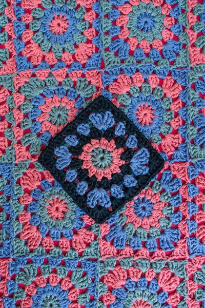 Granny square in black color as main placed on crochet afghan with same motifs. Contrast and texture of crochet patterns.