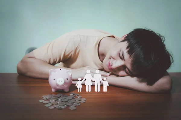 Handsome man is happy smiling and looking at icon family, piggy bank on the table, donation, saving, charity, family finance plan concept, fundraising, superannuation, investment, financial crisis concept