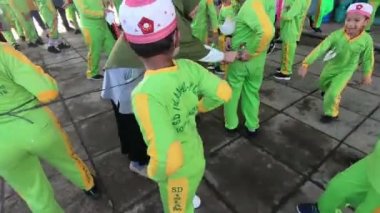 a rope to the waist of a child who will compete in a race to hammer nails into a bottle. This competition is for team coordination. 4K video footage. South Kalimantan, Indonesia. August 18, 2022.
