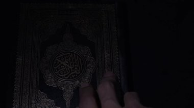 Müslüman kutsal kitabını açıyorum. Kitabın kapağında altın harfler var. Karanlık arka planda İslam 'ın kutsal yazıtları. 4K video görüntüleri. Güney Kalimantan, Endonezya. 17 Nisan 2023.