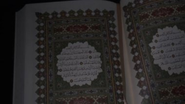 Müslümanların kutsal kitabını kapatıyorum. Kitabın kapağında altın harfler var. Karanlık arka plandaki kutsal İslam yazıtları. 4K video görüntüleri. Güney Kalimantan, Endonezya. 17 Nisan 2023.