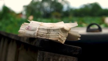 Rüzgarla savrulan ahşap bir yüzey üzerine bir yığın kağıt. Bulanık yeşil yapraklı bir arka planı var. 4K video görüntüleri.