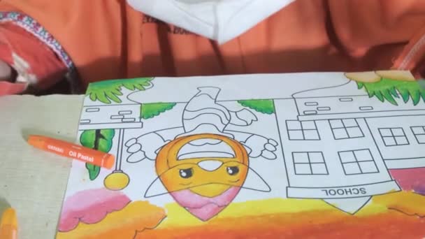 アジアの女の子がオレンジのクレヨンでキャラクターを着色しています 学校でのカラーレッスン キャラクターの顔と空を彩る 上からの眺め 学校でのカラーコンテスト — ストック動画