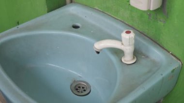 Kırmızı gömlekli Asyalı bir adam musluğu açmaya çalışıyor ama hiç su akmıyor. Su kaynaklarının kavramsal görüntüsü ya da arızalı tesisat. Tarafsız bir arkaplanda çekilmiş..