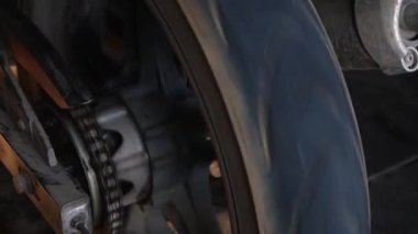 Çamur ve çamurla kaplı bir motosiklet lastiği ve zinciri görüntüsü. Bu yakın çekim motorun dayanıklı ve cesur halini yakalar, off-road maceralarına ve mekaniklere odaklanmış projeler için mükemmeldir. 4K