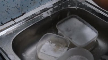 Mutfak lavabosundaki sabun köpüğünü temizlemek için bulaşıkları yıkayan bir adam. Su çatalların üzerinden akar ve temiz ve taze bir manzara yaratır. Mutfak işleri, temizlik ve ev işleri için mükemmel bir proje.