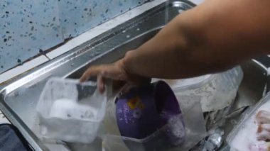 Mutfakta çalışan bir adam, sofra takımlarını temizliyor. Bulaşıkları ve çatal bıçakları sabun ve suyla yıkıyor, temizliği sağlıyor. Mutfak işleri, hijyen ve günlük ev işleri için mükemmel bir proje. 4K