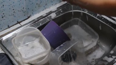 Restoran mutfağında çalışan Asyalı bir adam bulaşık ve kap kacak yıkıyor. Yoğun bir ortamda temizlik ve verimliliğe odaklanmış. Mutfak işleri, hijyen ve restoran 4K projeleri için mükemmel.