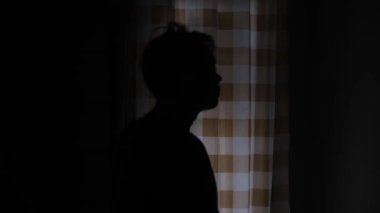 Kafası aşağıda ve omuzları çökmüş üzgün ve hayal kırıklığına uğramış bir adamın silüeti. Duruşu derin duygusal karışıklığı ifade ediyor, kasvetli ruh halini güçlendiren karanlık ışıkla daha da güçleniyor. 4K 