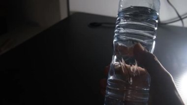 Bir adamın eli bir şişe maden suyunu kaldırır ve döndürür. Açık hareket etiketi ve şekli vurgular. Ürün sunumu, sağlık temaları, hidrasyon ve reklam görselleri için mükemmel