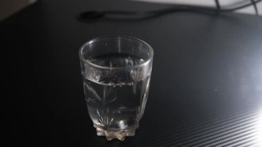 İçi maden suyu dolu bir bardak ve siyah bir masaya yerleştirilmiş yarım şişe. Kontrastlı açık kompozisyon, hidrasyon, ürün tanıtımı, sağlıklı yaşam tarzı ve içecek için ideal. 4K