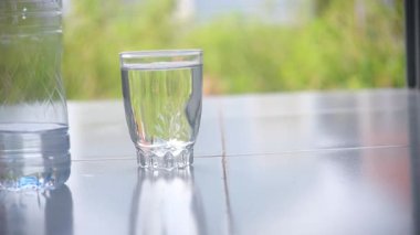 Şişeden temiz bir bardağa maden suyu dökerek şişeyi onun yanına koyuyor. Doğal bulanıklığı olan ferahlatıcı ve minimal bir sahne, sağlık, su ve yaşam tarzı temaları için ideal. 4K