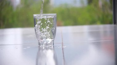 Doğal olarak bulanık arkaplanı olan temiz bir bardağa maden suyu dökmek. Ferahlatıcı ve temiz sahne, sağlıklı yaşam tarzı, su, içecek görselleri ve ürünle ilgili içerik için ideal. 4K