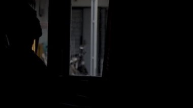 Sandalyesinden kalkıp yatak odasının penceresinden uzaklaşan bir adamın silüeti. Barışçıl ama duygusal bir an, ayrılışı, değişimi ya da derin düşüncenin sonunu simgeliyor. 4K görüntüler. video