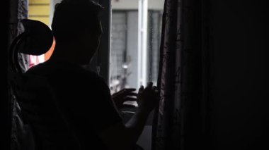 Sandalyeye oturmuş, hayal kırıklığı içinde arkasına yaslanmış, sonra da yatak odasının penceresinden uzaklaşan bir adamın silüeti. Stres, üzüntü ve duygusal yoksunluk, sakin bir anda. 4K görüntüler. video