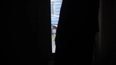 Pencerenin önünde duran bir adamın silueti, sessizce dışarı bakıyor, sonra da uzaklaşıyor. Sakin sabah ışığı, içe dönük ruh hali, yumuşak doğal ışıkla huzurlu bir ev sahnesi. 4K görüntü videosu. 