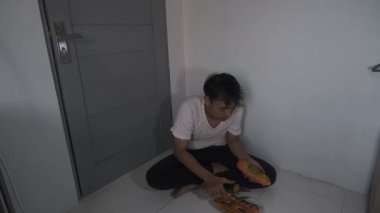 Kirli, pejmürde kıyafetler giyen evsiz bir Asyalı tek başına oturmuş, elleriyle olgun bir papayayı dikkatlice soyarken aç görünüyor. Sahne, yoksulluk ve açlığın saf ve duygusal bir anını yakalar.