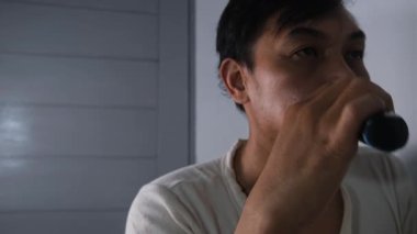 Eskimiş beyaz gömlek giyen Asyalı bir adam aynaya bakarken yüzünü elektrikli jilet kullanarak tıraş ediyor. Kamera onu önden yakalar, odaklanmış ifadesini ortaya çıkarır. video görüntüleri 4K