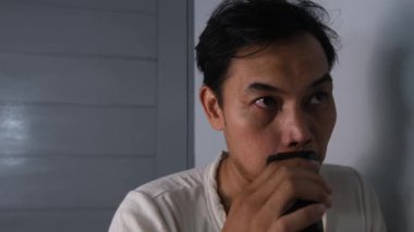 Beyaz gömlek giyen bir adam elektrikli jiletle bıyığını tıraş ediyor. Cihazı üst dudağına nazikçe bastırarak dikkatlice tımar etmeye odaklanıyor. Olay yeri temiz ve basit bir görüntü yakalıyor. 4K