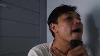 Giyinik fakir bir adam sakalını elektrikli tıraş makinesi kullanarak temizliyor. Odaklanmış ifadesi hijyeni korumak için gösterdiği özen ve çabayı gösteriyor. Sahne samimi ve gerçekçi bir anı vurguluyor. 4K