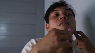 Asyalı bir adam hem jilet hem de elektrikli tıraş makinesi kullanarak yüzünü tıraş ediyor. Sahne, geleneksel ve modern araçları birleştirerek kişisel bakım ve hijyene odaklanan bir bakım rutinini gösteriyor. 4K