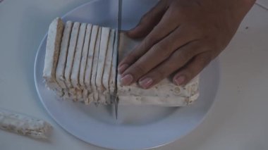 Tempeh 'in beyaz bir tabakta dilimlendiği yakın plan bir fotoğraf. Bir el, soya bazlı yoğun gıdaları dikkatlice keser ve sert dokusunu gösterir. Temiz arkaplan ve basit kompozisyon doğal olanı vurgular.