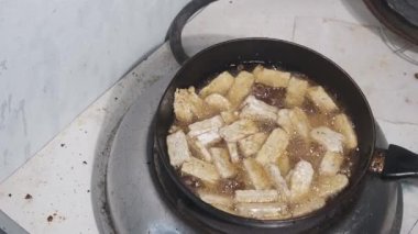 Çiğ beyaz tempeh dilimleri siyah bir tavada kızgın yağda kızartılıyor. Cızırdayan yağ taze soya bazlı gıdayı pişirmeye başlar ve soluk tempeh ile koyu tencere arasında kontrastlık yaratır. 4K