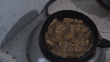 Tempeh, ocağın üstünde kızgın yağda kızartılıyor. Buhar ve kabarcıklar yükseldikçe altın dilimler cızırdıyor, geleneksel kızartmanın dokusunu ve sıcaklığını yakalıyor. Sahne özetleri. 4K