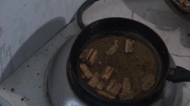 Bir el kavrulmuş fırtınayı kaldırmak için cızırdayan yağ tavasına uzanır ama dokunmadan önce durur ve geri çekilir. Sahne, yemek pişirirken tereddüt görüntüsünü yakalıyor ve bir an için tekrar gözden geçiriliyor. 4K